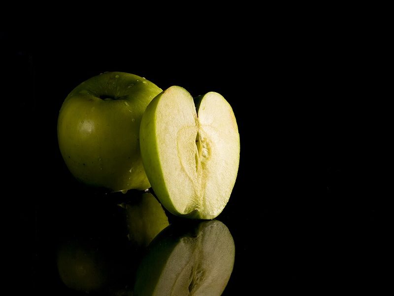 A green apple and a cut half on a black reflective surface