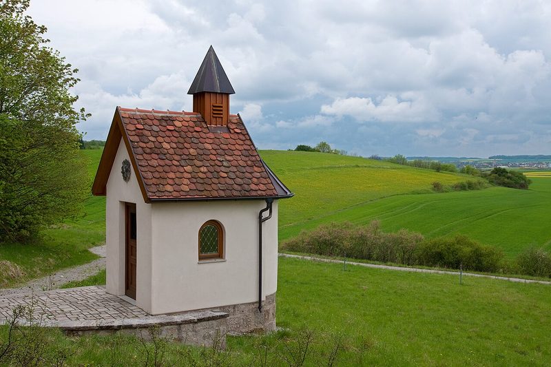 A small white chapel with a red tiled roof among green fields