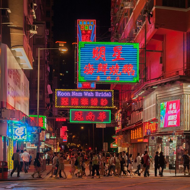 A crowded Hong Kong street at night under red and green neon signs