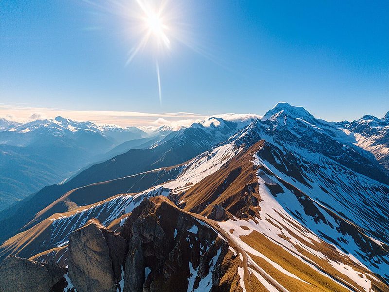 A snowy mountain ridge under a bright sun and a deep blue sky