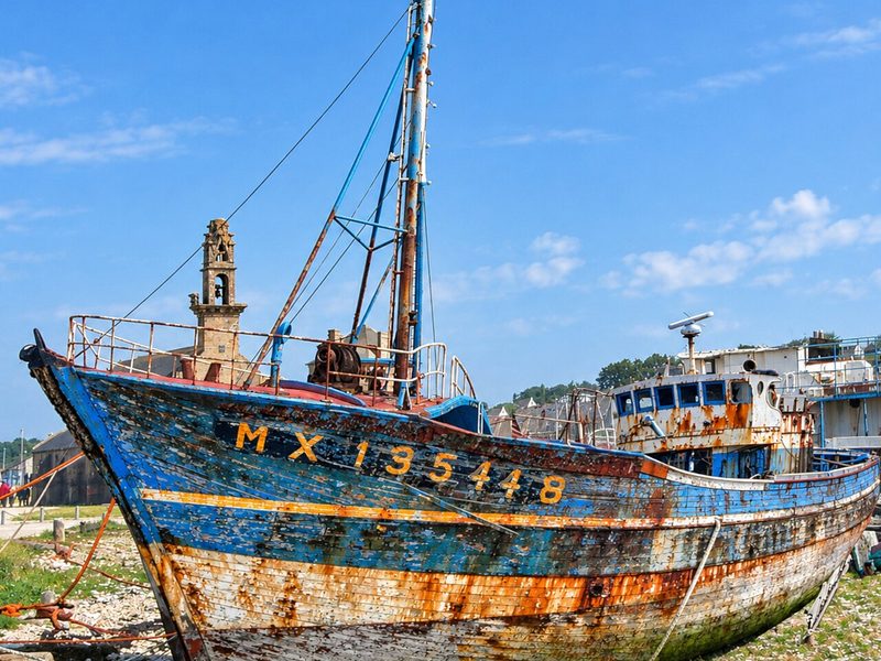 A rusty blue fishing boat with its registration number painted on the bow